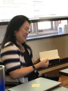 woman with dark hair holding a notebook and thumbing through the pages while smiling