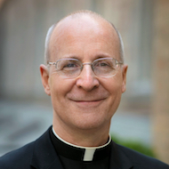 headshot of balding man with glasses smiling wearing a clerical collar