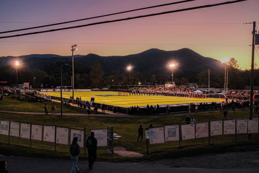 Dusk scene of football field with fans in stands and mountains in distance